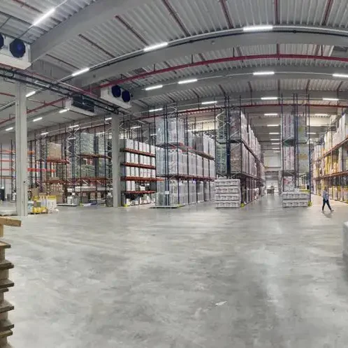 Isofit Shop Lager Großer Lagerraum mit Regalen voll mit Kisten und Waren, leerer Boden, Person in der Ferne.